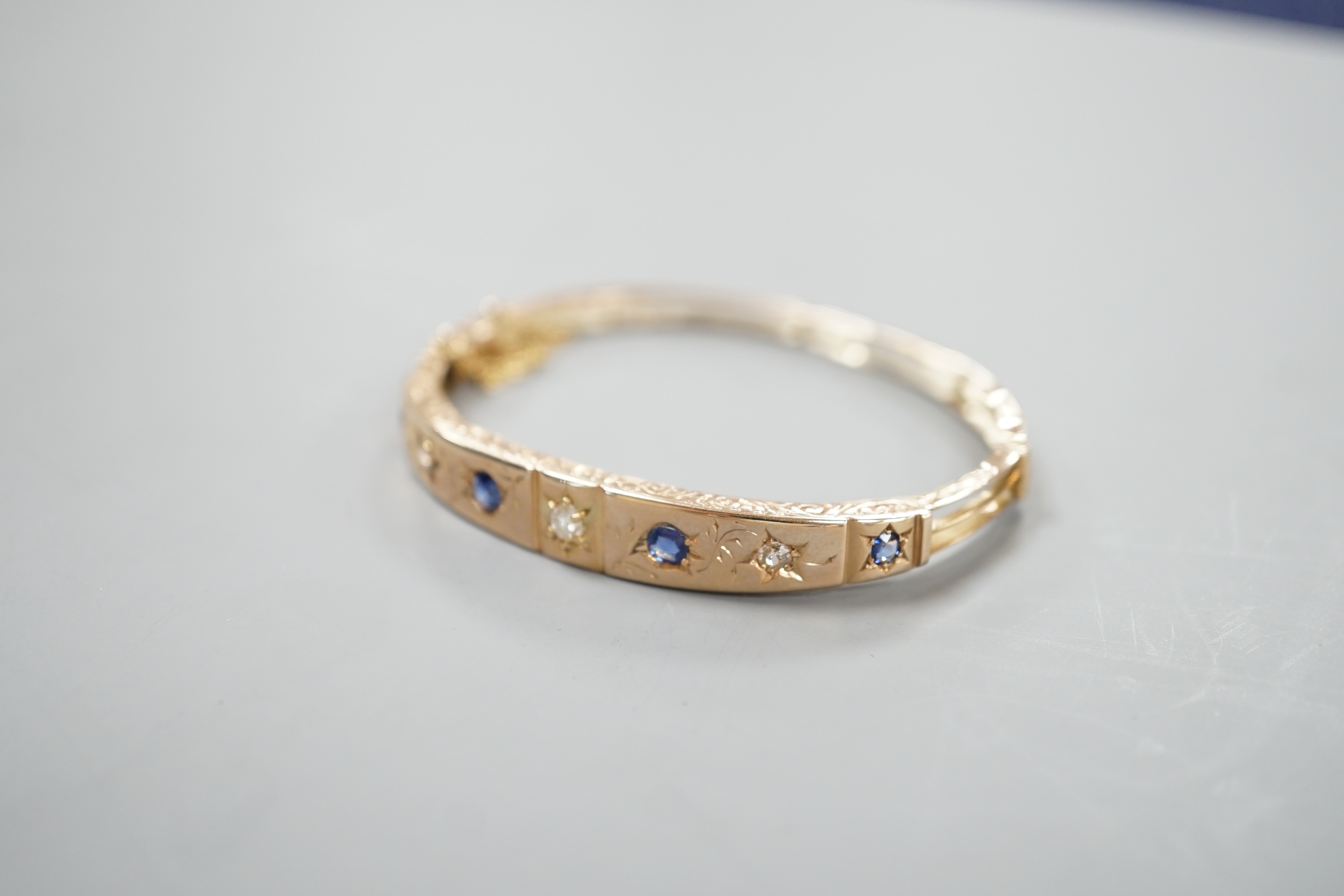 A late Victorian engraved yellow metal, four stone sapphire and three stone diamond set hinged bangle, gross 10.5 grams.